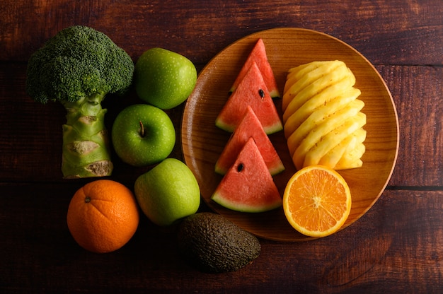 Pastèque, ananas, oranges, coupées en morceaux avec avocat, brocoli et pommes sur table en bois. Vue de dessus.