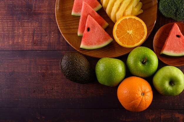 Pastèque, ananas, oranges, coupées en morceaux avec avocat, brocoli et pommes sur table en bois. Vue de dessus.