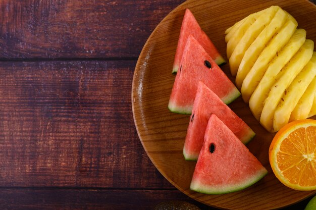 Photo gratuite pastèque, orange et ananas coupés en morceaux sur une plaque en bois