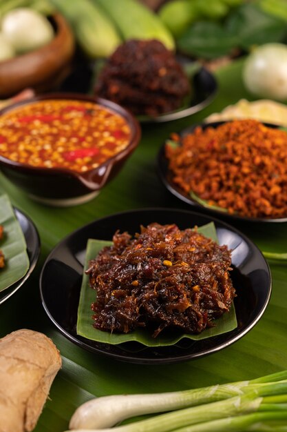 La pâte de chili est servie sur des feuilles de bananier dans une assiette avec des haricots longs, du citron vert, du chili et des aubergines.