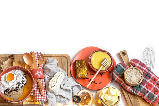 Pâte, différents couteaux et ingrédients pour les biscuits de Noël sur une table en bois blanche, à plat.