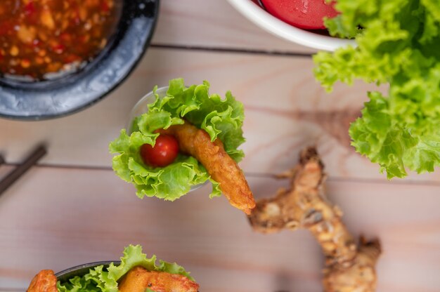 Pâte frite aux crevettes placée sur salade et tomates dans un bol en bois.