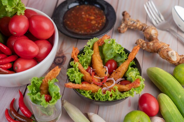 Pâte frite aux crevettes placée sur salade et tomates dans un bol en bois.