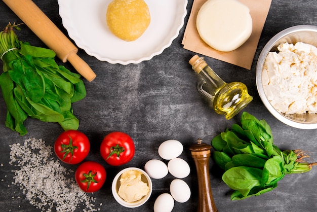 Pâte, huile, fromage, tomates, œufs, légumes verts sur une surface en bois grise