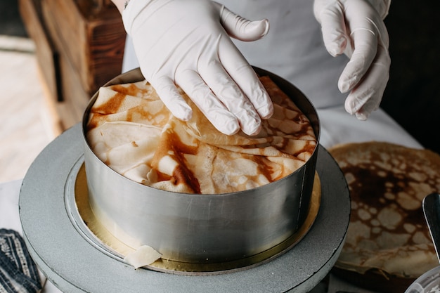 Pâte à l'intérieur de la poêle ronde avec cuisinier étalant des tranches de cuisson des repas sur elle à l'intérieur de la cuisine