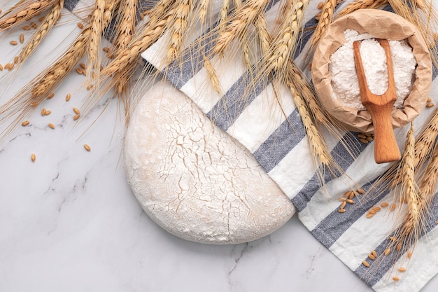 Pâte à levure fraîche faite maison reposant sur une table en marbre avec des épis de blé et un rouleau à pâtisserie.