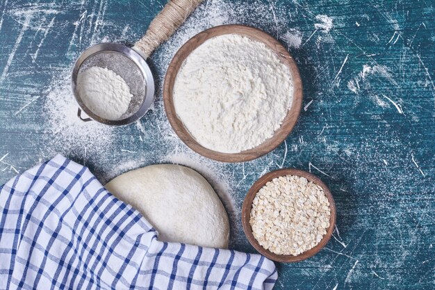 Pâte à pain avec des ingrédients sur table bleue.