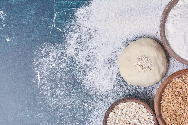 Pâte à pain avec des ingrédients sur table bleue.