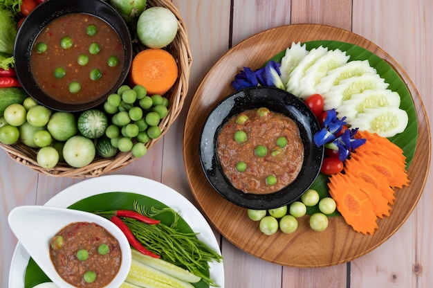 Photo gratuite pâte de pâte de chili dans un bol avec aubergine, carottes, piment, concombres dans un panier sur table en bois