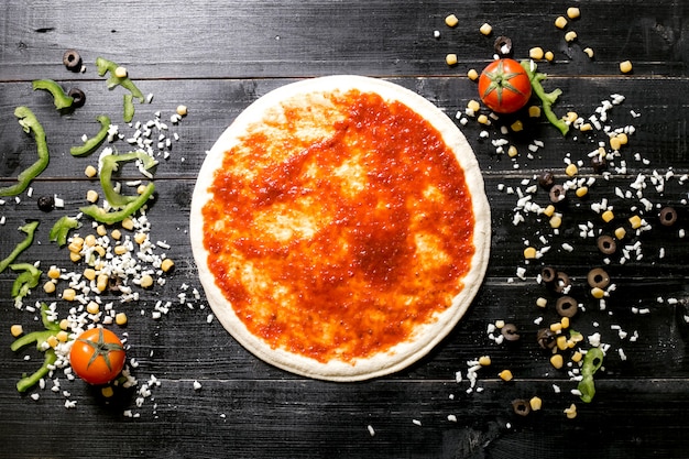 Pâte à pizza avec sauce tomate à côté de fromage arrose de maïs olive tomate poivron