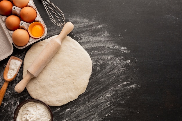 Photo gratuite pâte avec rouleau à pâtisserie et carton d'oeufs