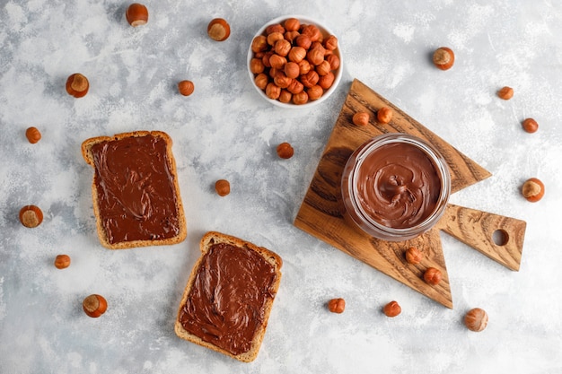 Pâte à tartiner au chocolat ou crème de nougat aux noisettes dans un bocal en verre sur du béton, fond