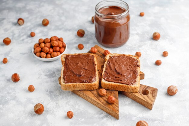 Pâte à tartiner au chocolat ou crème de nougat aux noisettes dans un bocal en verre sur du béton, fond