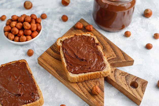 Pâte à tartiner au chocolat ou crème de nougat aux noisettes dans un bocal en verre sur du béton, fond