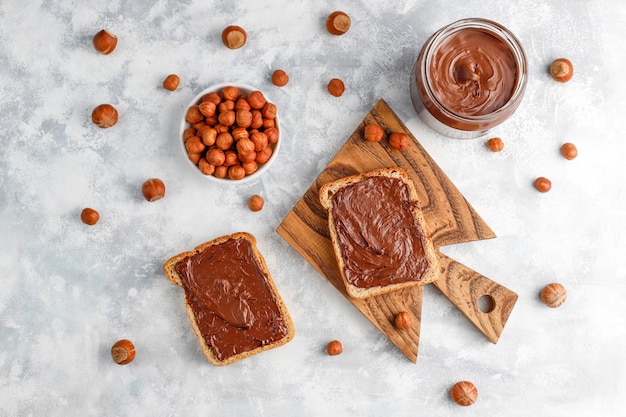 Pâte à tartiner au chocolat ou crème de nougat aux noisettes dans un bocal en verre sur du béton, fond