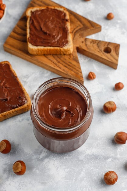 Pâte à tartiner au chocolat ou crème de nougat aux noisettes dans un bocal en verre sur du béton, fond