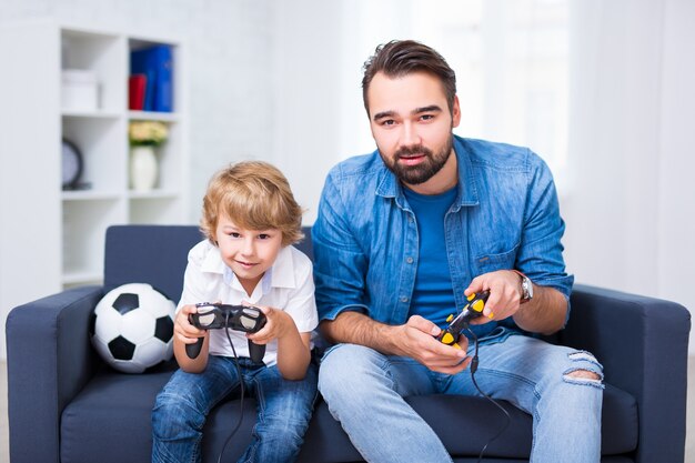 Paternité - père et fils assis sur un canapé à la maison et jouant au jeu vidéo