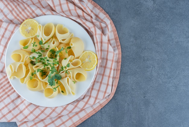 Pâtes bouillies avec des tranches de citron sur une plaque blanche.