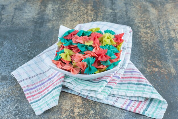 Pâtes colorées de noeud papillon dans le bol, sur la tour de thé, sur la surface en marbre.