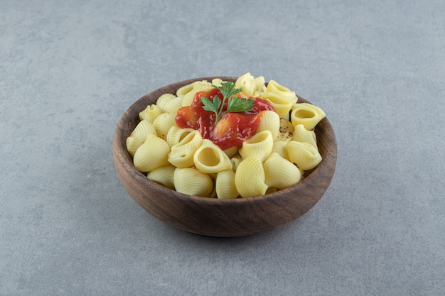 Pâtes conchiglie bouillies avec du ketchup dans un bol en bois.