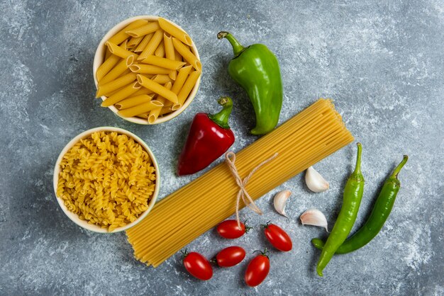 Pâtes crues aux légumes frais sur gris.