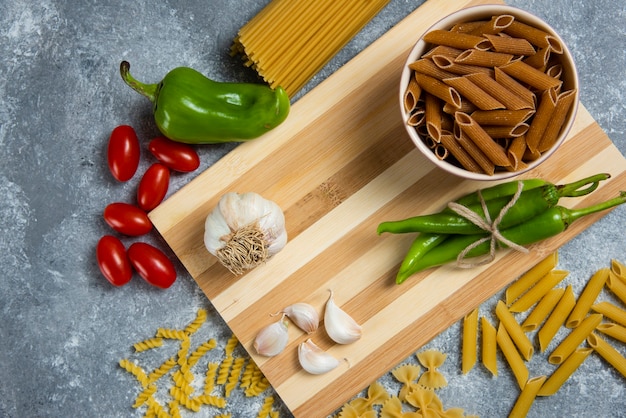 Pâtes crues aux légumes sur planche de bois.