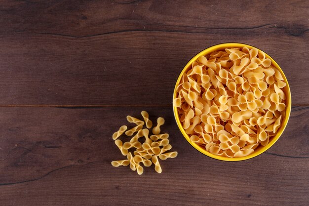 Pâtes crues dans le bol jaune vue de dessus sur la surface en bois