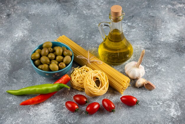 Pâtes crues, huile et légumes frais sur la surface de la pierre.