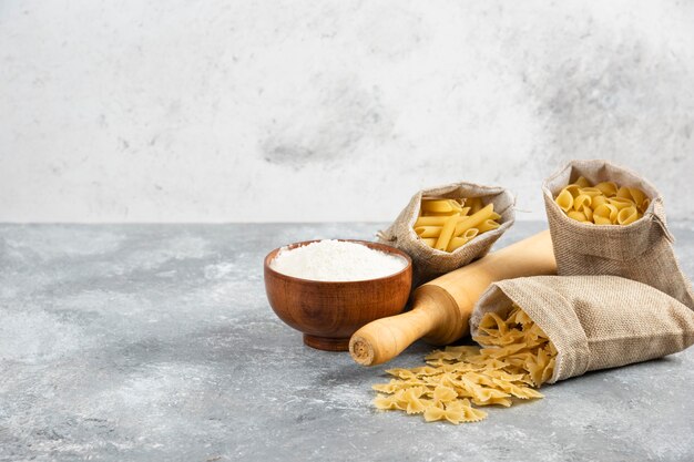 Pâtes dans un panier rustique avec rouleau à pâtisserie et une tasse de farine en bois autour.