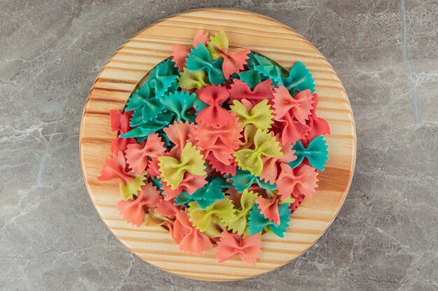 Pâtes farfalle colorées sur plaque de bois