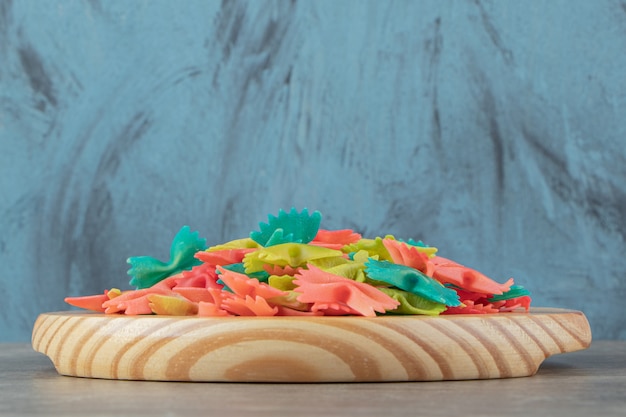 Pâtes farfalle colorées sur plaque de bois.