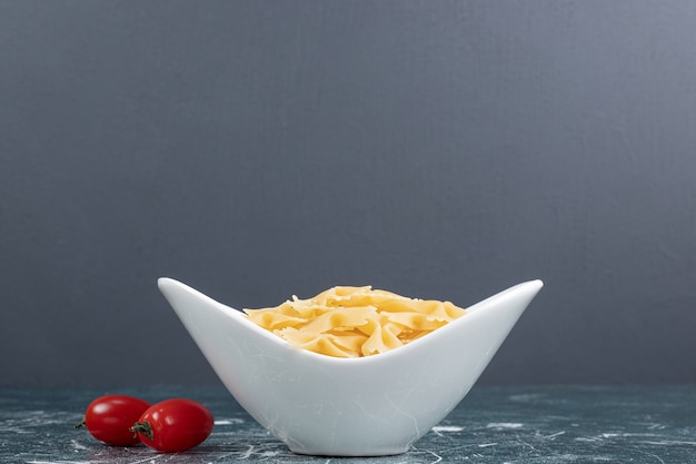 Pâtes farfalle crues dans un bol blanc et tomates. Photo de haute qualité