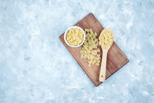 Pâtes farfalle dans un bol blanc et cuillère en bois sur fond grungy et planche à découper. vue de dessus.