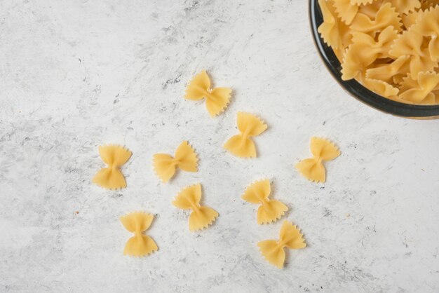 Pâtes farfalle dans un bol en verre sur fond blanc.