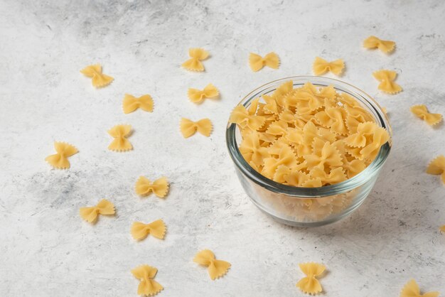 Pâtes farfalle dans un bol en verre sur fond blanc.