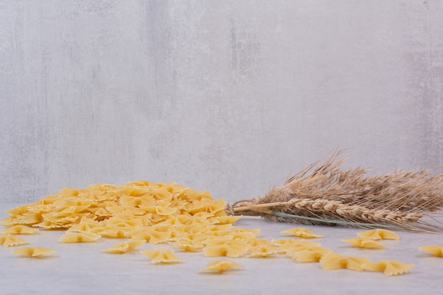 Pâtes farfalle non cuites sur une surface blanche avec du blé