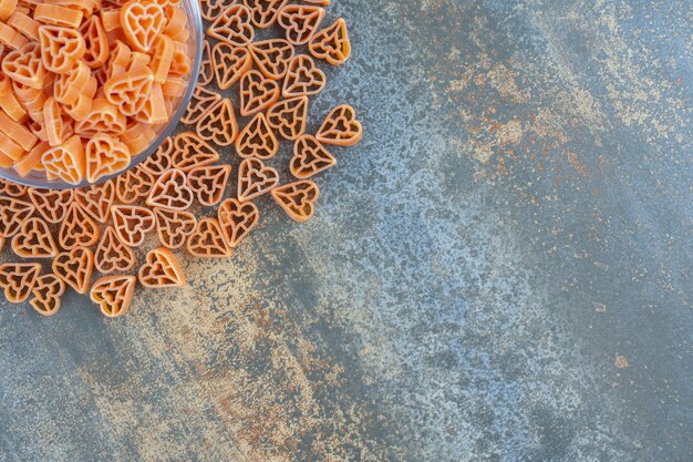 Pâtes en forme de cœur dans et autour du bol, sur la surface en marbre.