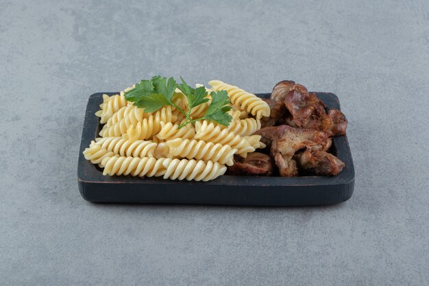 Pâtes fusilli au poulet sur plaque noire.