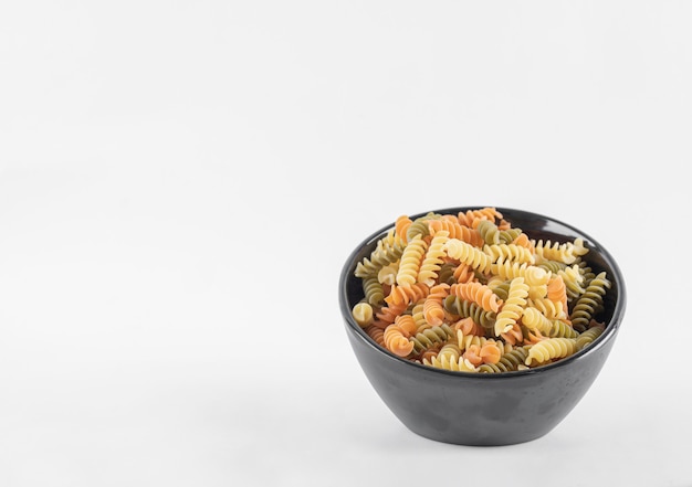 Pâtes fusilli colorées crues dans un bol sombre.