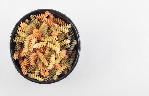 Pâtes fusilli colorées crues dans un bol sombre.