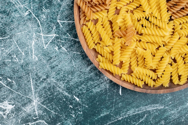 Pâtes fusilli cru jaune sur plaque de bois.