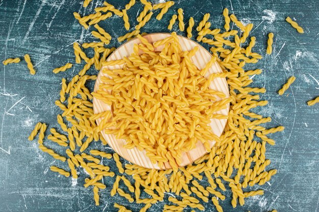 Pâtes fusilli cru jaune sur plaque de bois.