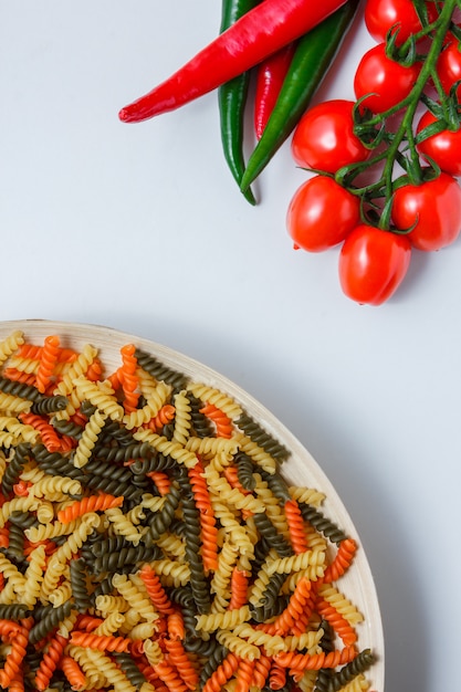 Pâtes fusilli dans une assiette de tomates, poivrons à plat sur un tableau blanc