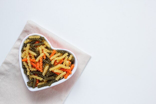 Pâtes fusilli dans un bol blanc sur table nappe blanche et pliée, vue du dessus.