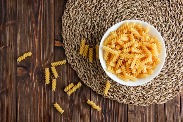 Pâtes fusilli dans un bol sur napperon en bois et osier, mise à plat.