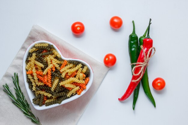 Pâtes fusilli dans un bol avec des poivrons, des tomates, des plantes vertes vue de dessus sur une table nappe blanche et pliée