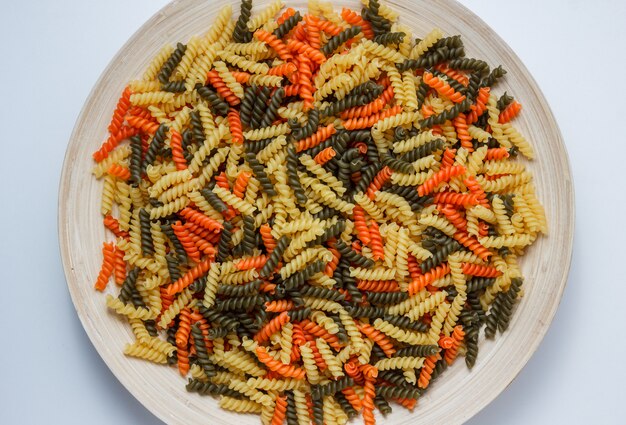 Pâtes fusilli non cuites dans une assiette sur tableau blanc, vue du dessus.