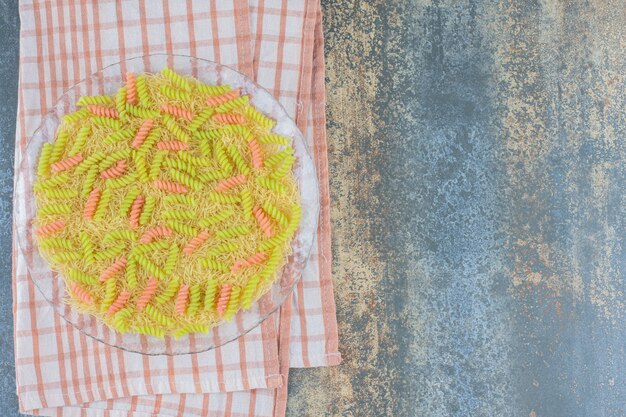 Pâtes fusilli non cuites dans le bol en verre, sur une serviette, sur le fond de marbre.