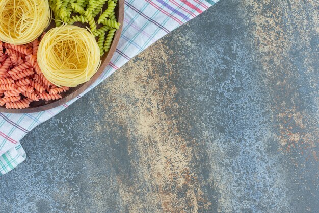 Pâtes fusilli rouges et vertes avec de fines spaghettis dans le bol sur une serviette, sur le fond de marbre.