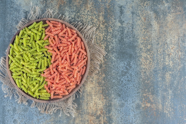 Pâtes fusilli vertes et rouges dans un bol sur une serviette, sur la surface en marbre.